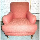 A modern club armchair, with red foliate upholstery on turned wooden supports and brass castors.