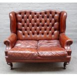 An 18th century style studded brown leather upholstered two seat wing back sofa on squat cabriole