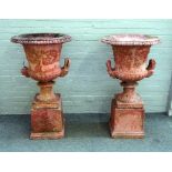 A pair of red glazed reconstituted stone, twin handled garden urns on square pedestals,