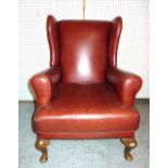 A 20th century mahogany framed wingback armchair with red leather upholstery on tapering cabriole