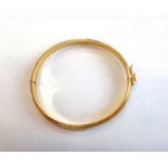 A gold oval hinged bangle, having a textured finish, on a snap clasp, with a foldover safety catch,