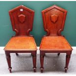 A pair of late George III mahogany hall chairs, each with shield shaped back and solid seat,