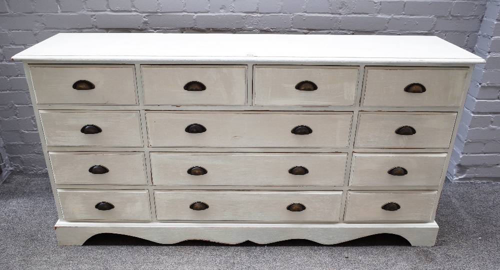 A 20th century off-white painted pine chest of thirteen various drawers, on shaped plinth,