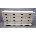 A 20th century off-white painted pine chest of thirteen various drawers, on shaped plinth,