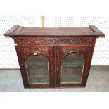 An early 20th century rosewood display cabinet with arch panelled glass doors and carved decoration,