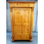 An early 20th century pine armoire with single door flanked by fluted pilasters on bun feet,