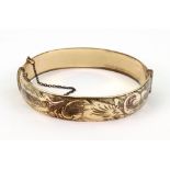 A gold hinged bangle, engraved with a scrolling foliate design, stamped 9CT,