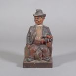 A tyrolean carved wood seated figure of a man, with music box inset.