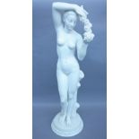 A modern alabaster/composite statue of a nude female holding a garland of flowers on a naturalistic