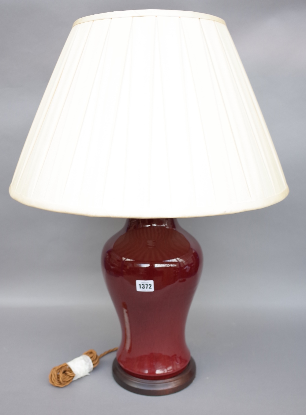 A Chinese porcelain vase table lamp, sang de boeuf, baluster ground with a cream silk pleated shade,