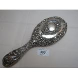 A heavily embossed silver hand mirror decorated with Swiss scrolls and flowers,