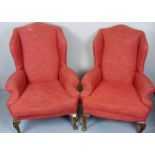 A pair of Victorian winged armchairs upholstered in salmon material and terminating on carved legs