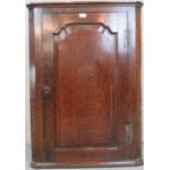 A George III oak corner cupboard with panelled arched door and three shelves to interior,