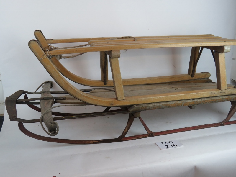 A pair of vintage wooden sledges with steel runners, the larger has an ankle steering mechanism,