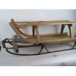 A pair of vintage wooden sledges with steel runners, the larger has an ankle steering mechanism,