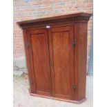 A Georgian mahogany corner cupboard with a carved frieze over double doors revealing two internal