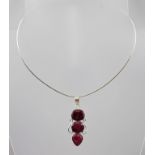 A SILVER THREE STONE PENDANT with chain, mounted with three facet cut ruby coloured stones