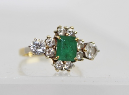 A DIAMOND AND EMERALD DRESS RING, the central facet cut emerald framed by eight small diamonds and