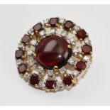 A DIAMOND SET BROOCH of "starburst" form, emanating from a central cabochon, the outer band set with