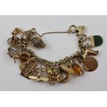 A 9CT GOLD CHARM BRACELET with padlock clasp, set with many and varied charms, some marked 9ct gold,