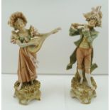 A PAIR OF ROYAL DUX PORCELAIN FIGURES of musicians in 18th century costume, raised on domed