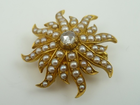 A STARBURST DESIGN BROOCH with pendant fitting, set with central diamond surrounded by seed