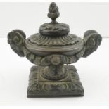 A 19TH CENTURY REGENCY DESIGN BRONZE URN WITH COVER, cast rams head handles on square platform base,