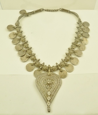 A BEDOUIN WHITE METAL NECKLACE decorated with coins, alternating with flower heads, suspending a