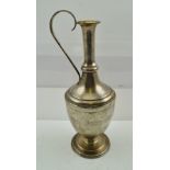 A FOREIGN SILVER COLOURED METAL CARAFE having slender ringed neck, floral engraved cup, belly and