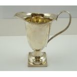 J** P** C** A CREAM JUG of helmet form, having reeded scrolling handle, on square plinth base,