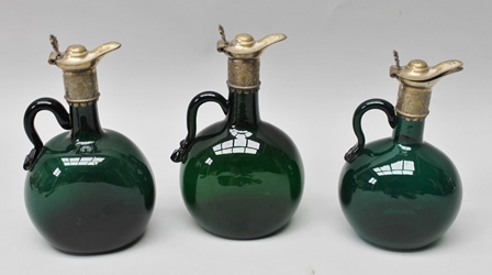 A GRADUATING TRIO OF GEORGIAN GREEN GLASS SPIRIT JUGS with plated mounts, (two with original