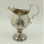 A GEORGE III SILVER CREAM JUG, having embossed swag decoration, on domed platform base, London 1780,