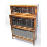 AN EARLY 20TH CENTURY OAK FINISHED GLOBE WERNICKE STYLE THREE-TIER BOOKCASE, having lift-up leaded