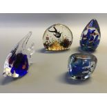 Four glass paperweights in various shapes with fish designs.
