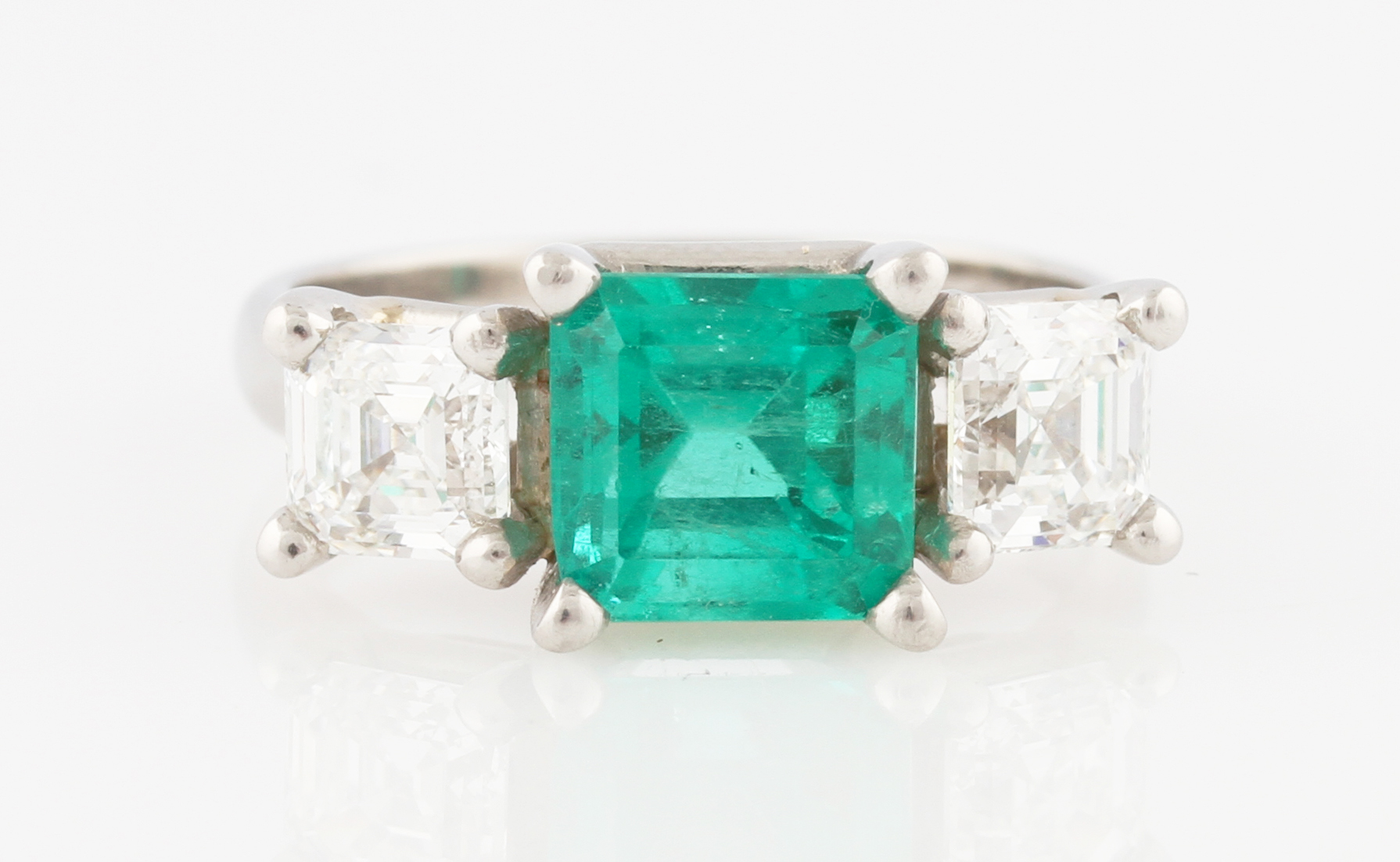 A platinum emerald and diamond three stone ring, the central emerald cut emerald measuring approx.