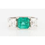 A platinum emerald and diamond three stone ring, the central emerald cut emerald measuring approx.