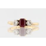 A ruby and diamond three stone ring, set with a central emerald cut ruby, measuring approx. 5x3mm,