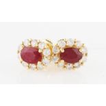 A pair of 18ct yellow gold ruby and diamond cluster stud earrings, each set with an oval cut ruby (