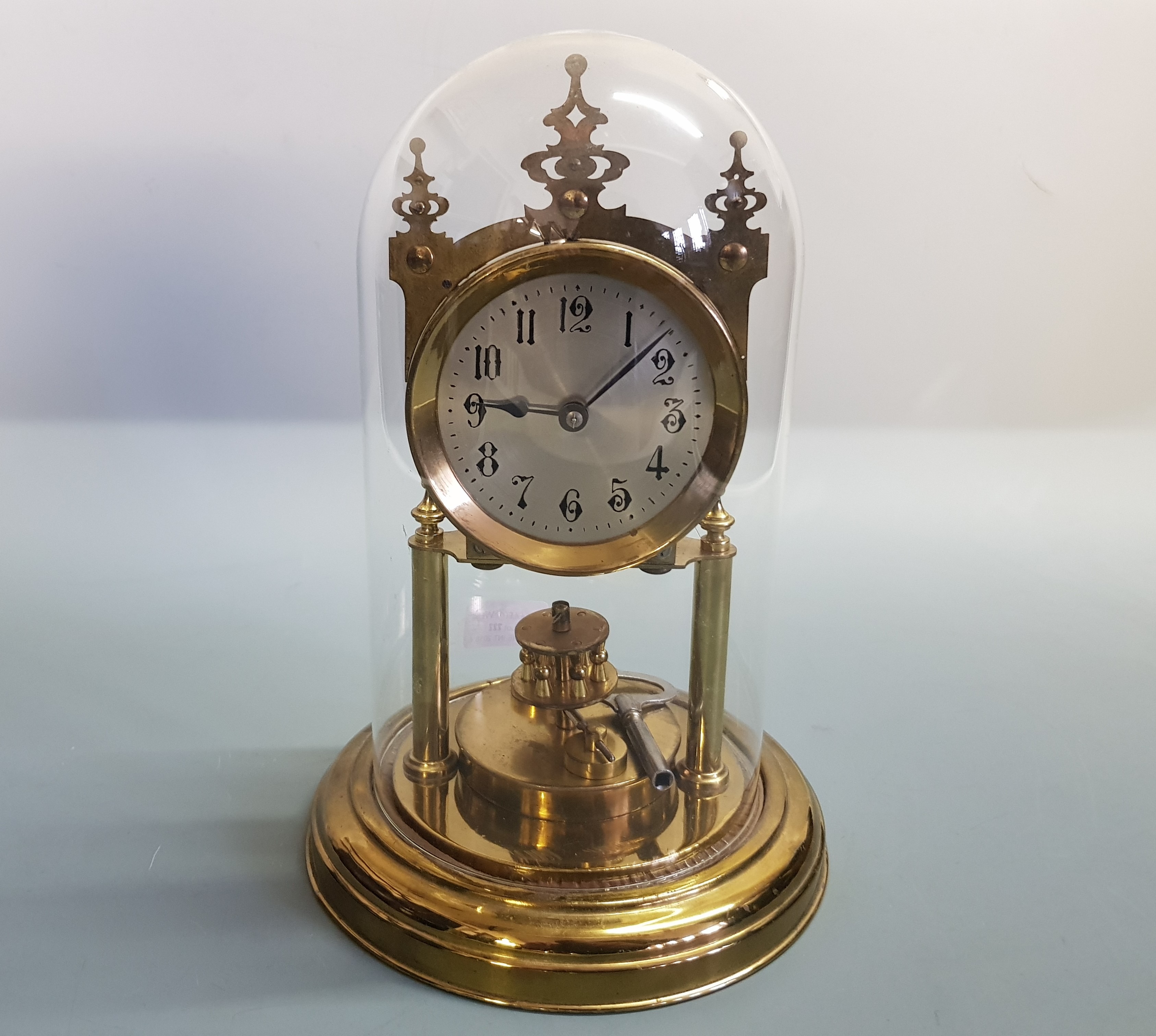 A brass anniversary mantle clock under glass dome.