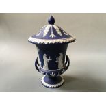 A Wedgwood dark blue and white two handled urn with lid and Greek goddesses, height 24cm.