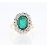 An emerald and diamond cluster ring, set with an oval cut emerald, measuring approx. 10x8mm,