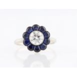 A diamond and sapphire flower design ring, set with a central transitional cut diamond, measuring