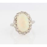 An opal and diamond cluster ring, set with a central oval opal cabochon measuring approx. 14x9mm,