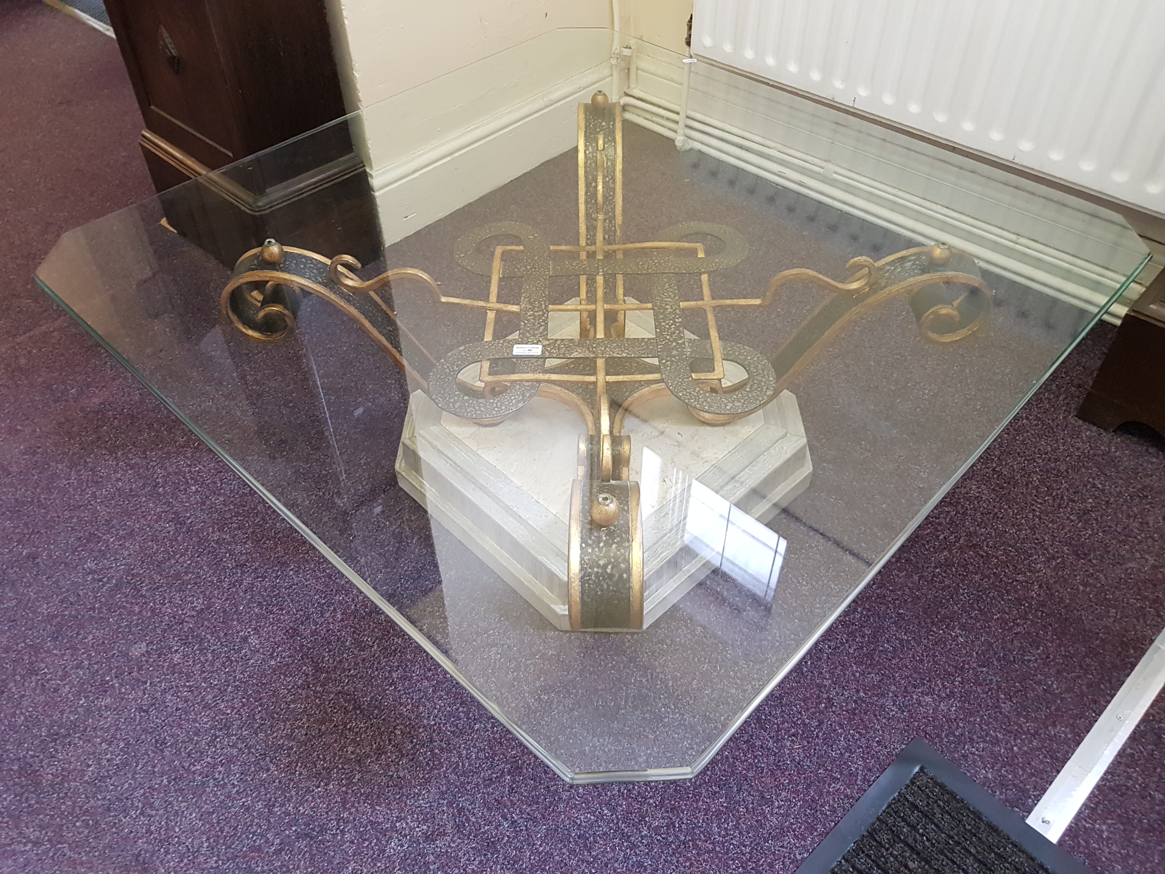 A beige and grey marble square coffee table with cast iron cross support on square glass top.