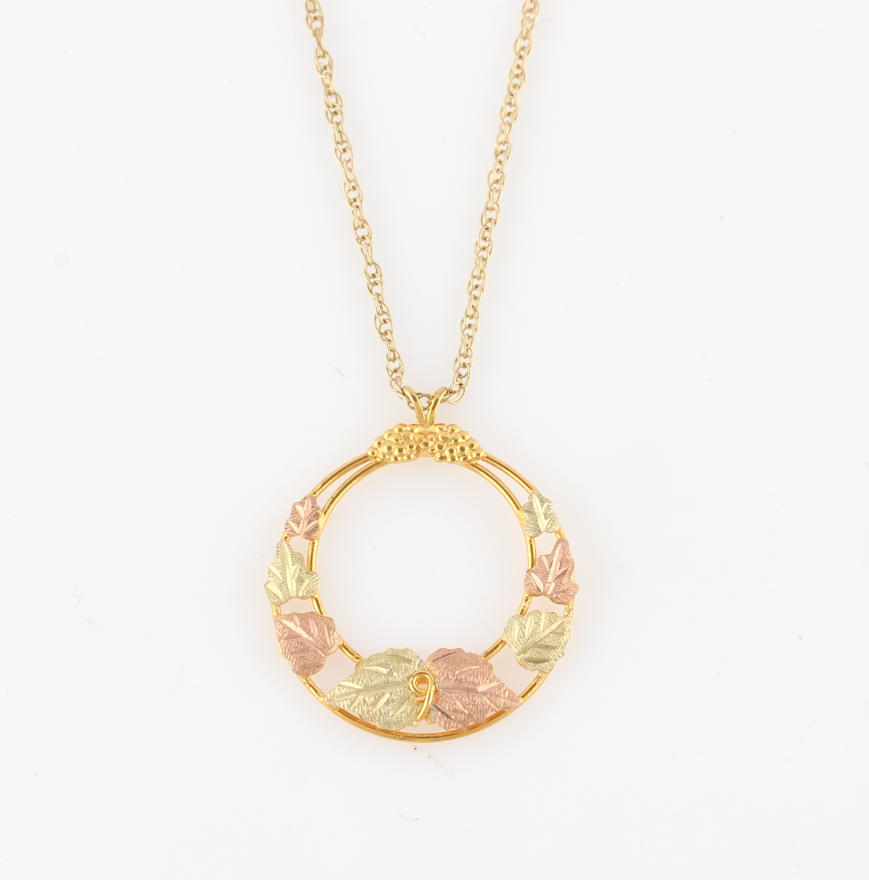 A 9ct two-tone gold pendant, of circular open metalwork design featuring leaves, hallmarked London