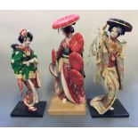 Three Geisha cloth coats figurines on stands.