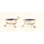 A pair of Victorian silver salts, both of circular design raised on three claw feet, with blue glass