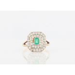 An Art Deco style emerald and diamond cluster ring, set centrally will an emerald cut emerald,