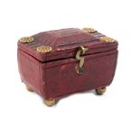 A Regency red leather needle packet box of sarcophagal form on gilt ball feet, the hinged top with