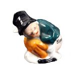 A porcelain novelty tape measure in the form of a man in black hat and green coat, crouching with